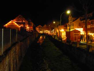 Chrischchindlimarkt Schlaate There are various illuminated market stalls on a road along a stream.