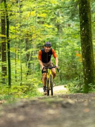 Ein Mann mit einem gelben Gravelbike fährt auf einem Naturweg durch den Wald.