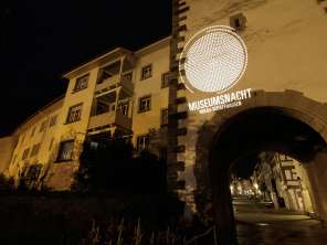 Museum Night Hegau-Schaffhausen An old town facade with an archway at night. The façade is illuminated with the slogan "Museumsnacht Hegau-Schaffhausen.