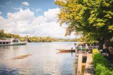 The regular boat service operates on the Rhine. Many people are sitting in a café on the riverbank.