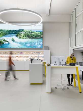 Visitor Centre Schaffhausen This is the counter area of the Schaffhausen Visitor Center. A woman in a mustard yellow sweater is standing at a high table talking on the phone. Another person walks to the free counter.