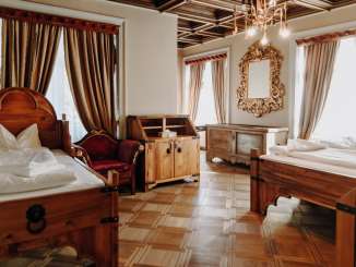 An overnight room with a wooden floor, several striking wooden beds, a golden mirror