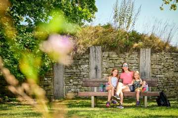 A mother sits on a wooden bench with her two daughters.