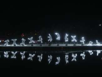 A light installation depicting a person jumping. The outline glows and is reflected in the Rhine.