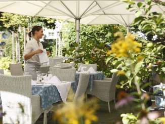 Garden villa Sommerlust A flowering restaurant garden is furnished with woven tables and chairs. The tables are set.